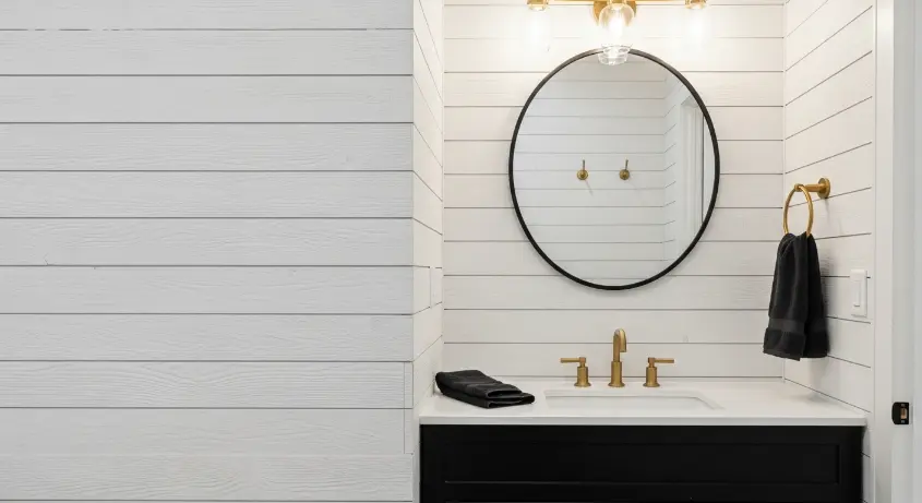 bathroom with a textured shiplap wall in white, a black vanity, and gold fixtures