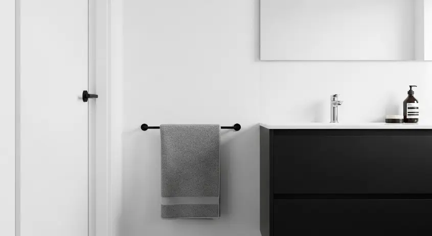 A minimalist bathroom with white walls, a black vanity, and a single gray towel.